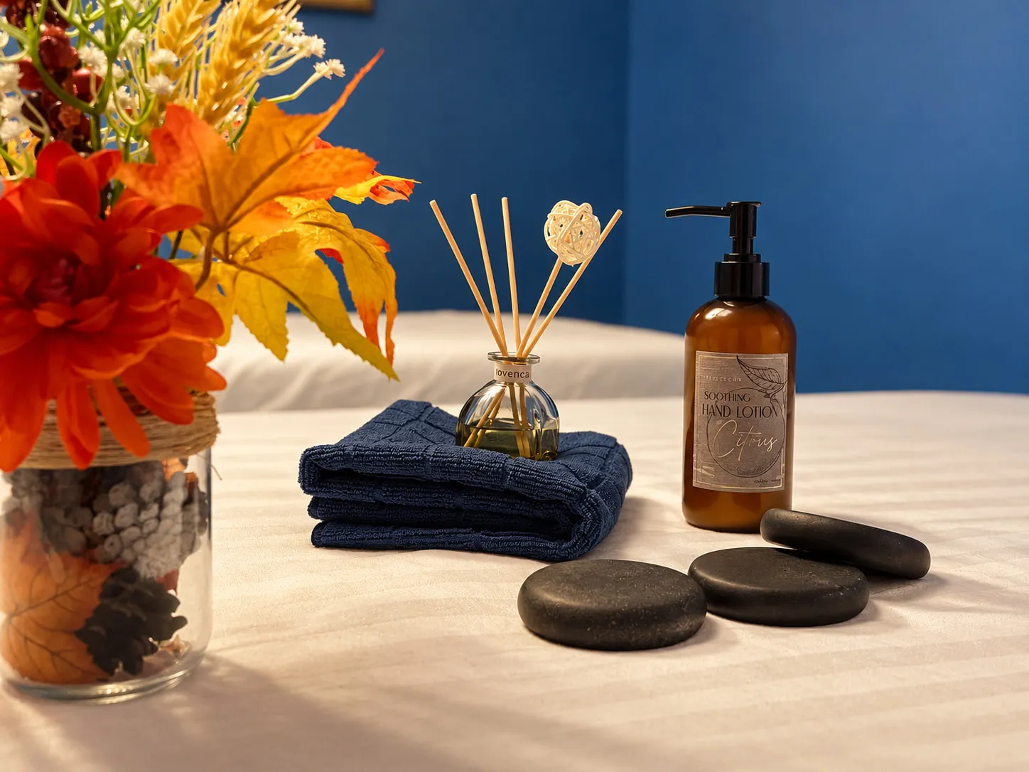 Folded towel, reed diffuser, lotion and smooth stones on a massage table at Wellness Massage Spa